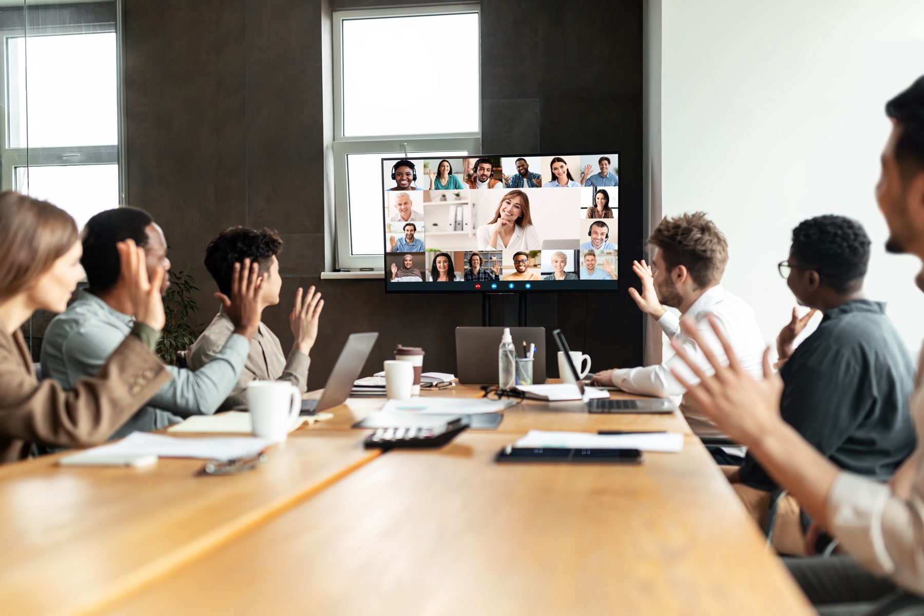 Team applaudiert bei einer hybriden Videokonferenz im Meetingraum – AGILean Academy